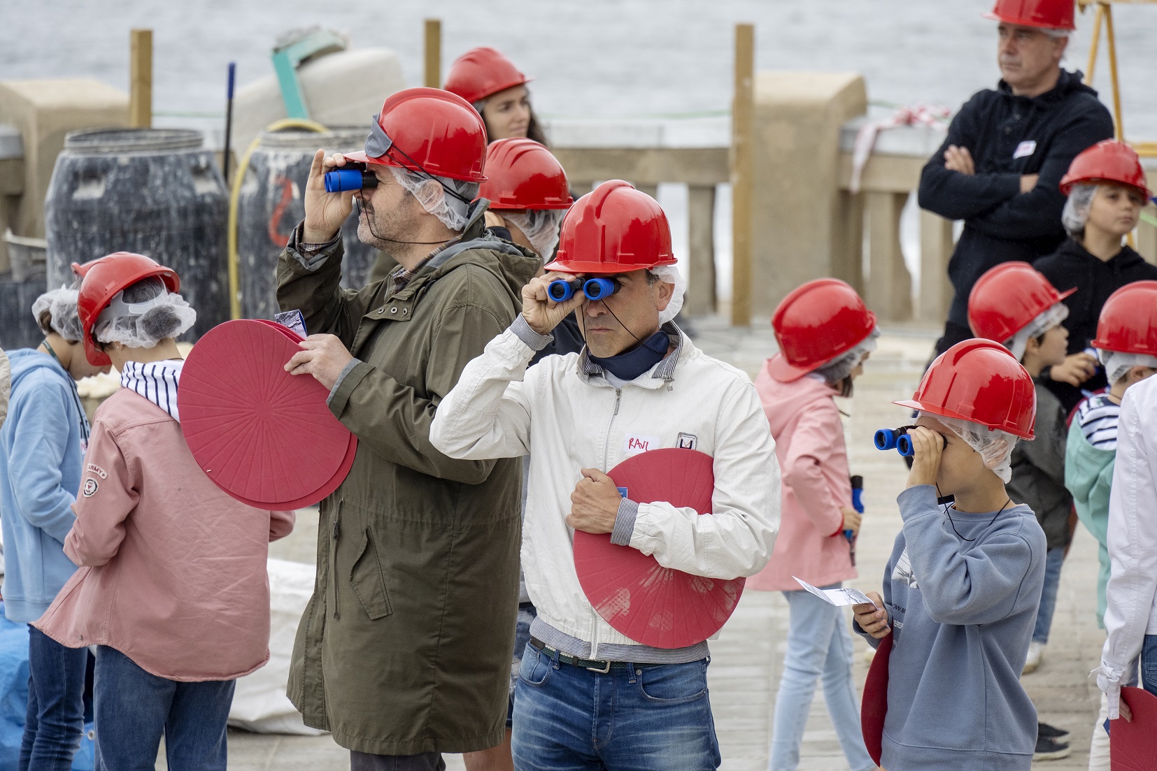 Adultos y menores con prismáticos y cascos de obra miran el paisaje de Punta Begoña